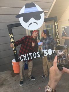 two people standing in front of a house with a sign that says happy birthday to them