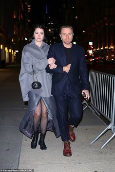 a man and woman are walking down the street at night, dressed in dark clothes