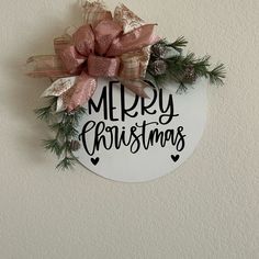 a merry christmas ornament hanging on the wall with pine cones and ribbon around it