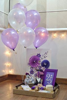 purple and white balloons are in the air above a table with gifts, flowers and decorations