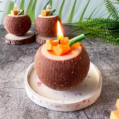 two coconuts with candles in them on a plate next to some plants and leaves