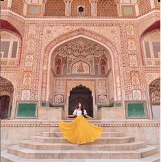 a woman in white shirt and yellow skirt standing on steps with stairs leading up to an ornate building