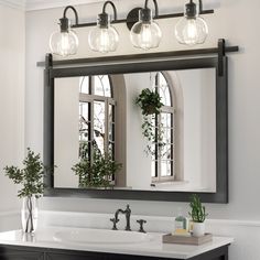 a bathroom vanity with three lights and a mirror above it, along with a potted plant