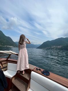 a woman standing on the bow of a boat looking out at mountains in the distance