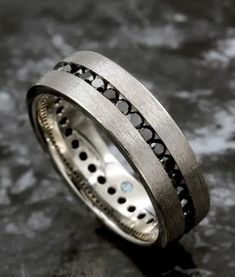 a wedding ring with black diamonds in it sitting on a stone slabd surface, ready to be used as a jewelry piece