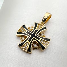 a black and gold cross pendant with white diamonds on the bottom is sitting on a white surface