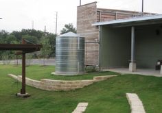 a large metal tank sitting on top of a lush green field next to a building