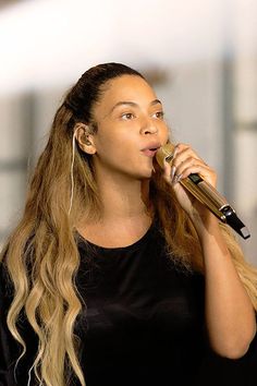 a woman with long hair holding a microphone in her right hand and wearing ear buds