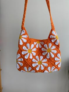 an orange purse with white flowers hanging from it's side on a hook in front of a wall