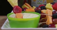 fruit skewers are arranged on a white plate with green cups and strawberries