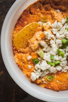 a white bowl filled with mexican food on top of a wooden table next to a fork