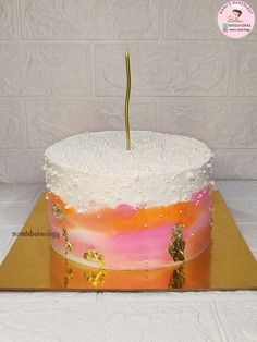 a cake with white frosting and pink and orange designs on it, topped with a single gold - dipped toothpick