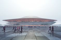 many people are walking around in front of a large building that has a curved roof