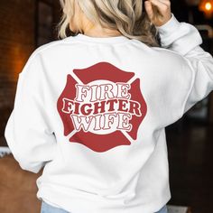 a woman wearing a white sweatshirt with the words fire fighter wife printed on her back