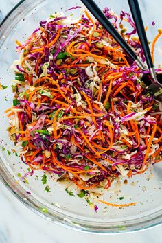 shredded carrots and red cabbage in a glass bowl with tongs on the side