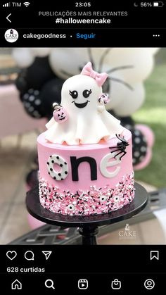 a cake decorated with pink and white frosting on top of a black stand in front of balloons