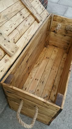 an empty wooden box sitting on the ground next to a brick wall with rope hanging from it