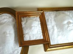 two gold frames sitting next to each other on top of a white sheet covered bed