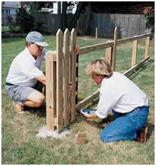 two men working on a wooden fence in the yard, one man is kneeling down