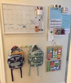 two backpacks are hanging on the wall in front of a calendar and bulletin board