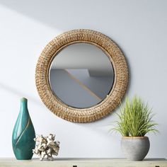 a round mirror hanging on the wall above a table with two vases and a potted plant