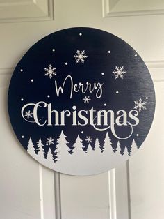 a merry christmas sign hanging on the front door with snowflakes and evergreen trees