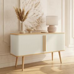 a sideboard with a plant and vase on it in front of a white wall