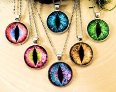 six different colored eyeball necklaces hanging from chains on a wooden surface with plants in the background