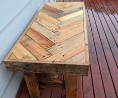 a wooden table sitting on top of a wooden floor next to a white house with red siding