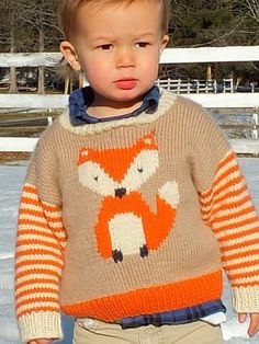 a little boy standing in the snow wearing a sweater with a fox on it