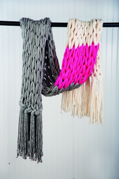 two knitted scarves hanging on a clothes line with white and pink yarns