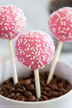 pink cake pops with white sprinkles in a cup filled with coffee beans