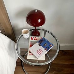 a glass table topped with books next to a lamp on top of a wooden floor