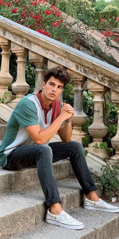 a young man sitting on the steps in front of some stairs with flowers behind him