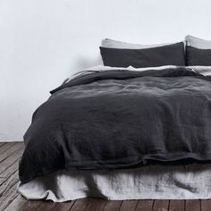 an unmade bed with black linens and white sheets in a room that has wood flooring