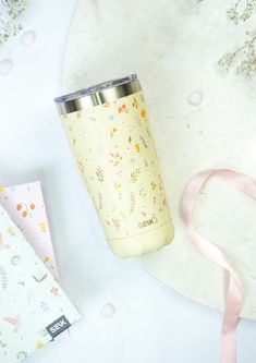 a yellow tumbler next to a pink ribbon on a white table with other items