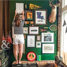 a woman standing in front of a green wall with pictures and deer heads on it