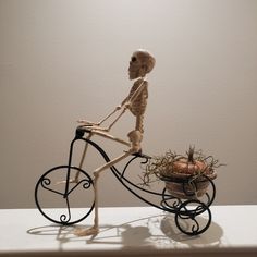 a skeleton riding a bike with a basket full of pumpkins