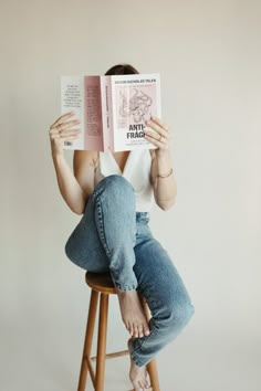 a woman is sitting on a stool and reading an anti - fragilian book