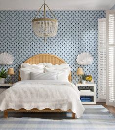 a bedroom with blue and white wallpaper, a wicker headboard, an upholstered bed, two nightstands, and a chandelier hanging from the ceiling