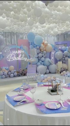 a table set up for a birthday party with balloons, plates and napkins on it