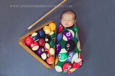 a baby is sleeping in a pool case with billiards on the floor next to it