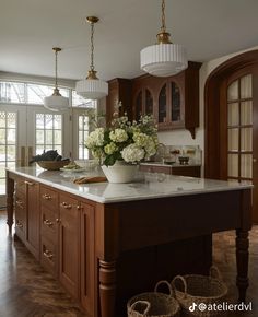 a large kitchen with wooden cabinets and white flowers in a vase on the center island