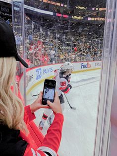 a woman taking a photo of an ice hockey game with her cell phone in front of the goal