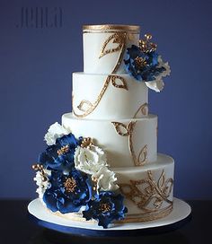 a three tiered wedding cake with blue and white flowers on the bottom, gold detailing