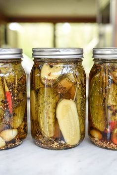 three jars filled with pickles sitting on top of a white counter next to each other