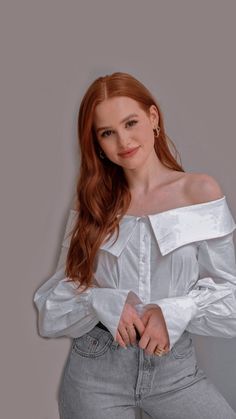 a woman with long red hair wearing a white shirt and jeans, posing for the camera