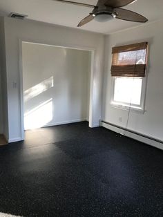 an empty room with a ceiling fan and window in the corner on the far wall