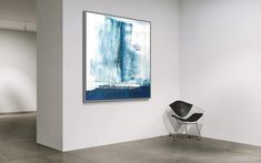 an abstract painting hangs on the wall next to a chair in a white walled room