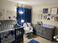 a baby's room with blue and gray decor on the walls, crib bedding and dressers